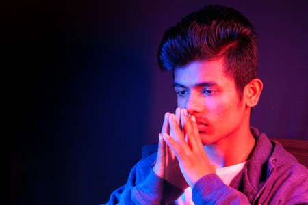 thoughtful young man sitting on chair at nightの写真素材