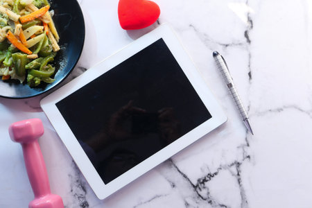 digital tablet , dumbbell and salad on plate