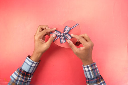 man hand holding heart shape gift box on red backgroundの写真素材