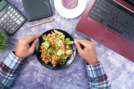 young man eating fresh salad while working on laptop