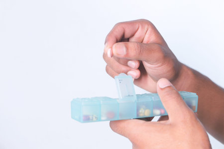 mans hands taking medicine from a pill box isolated on white