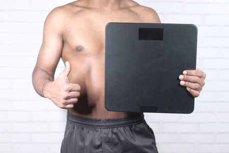 young man holding weight machine doing thumbs up signの写真素材