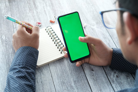 rear view of young man using smart phone and writing on notepad