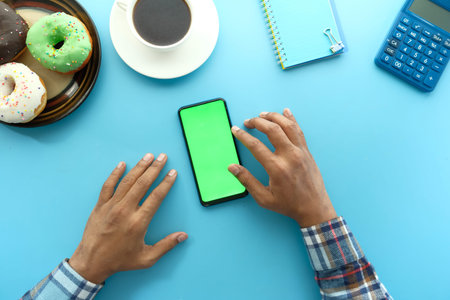 top view of man hand using smart phone with donuts, tea blue backgroundの写真素材