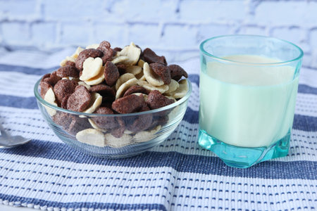 chocolate corn flakes in a bowl and milk on tableの写真素材