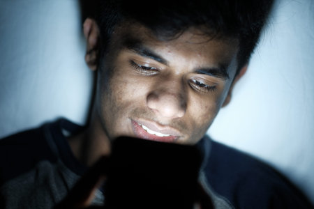 young man sitting on bed using smart phone at night