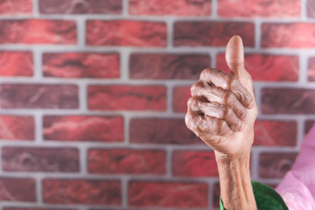 senior women hand showing a thumb-up against a wall