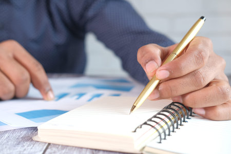 man hand with pen analyzing financial data and writing on notepad