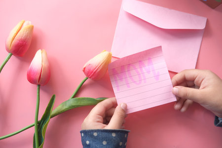 Top view child hand holding mother day gift and flower on pink.の写真素材