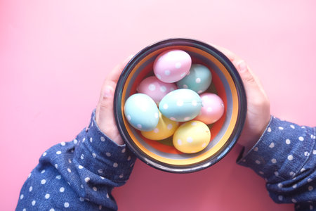 child hand holding a bowl of easter eggs on pinkの写真素材