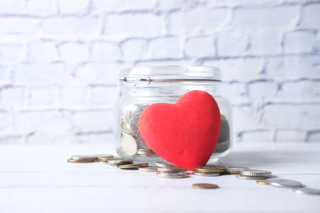 Red heart and coins in a jar on blue backgroundの写真素材