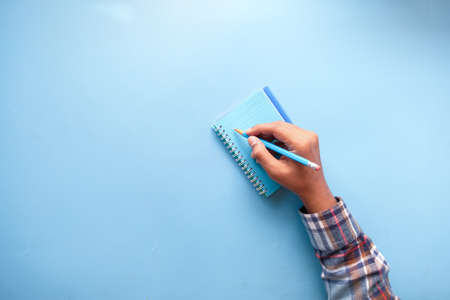 top view of man hand writing on notepad on blue backgroundの写真素材