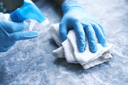 hand in blue rubber gloves holding spray bottleの写真素材