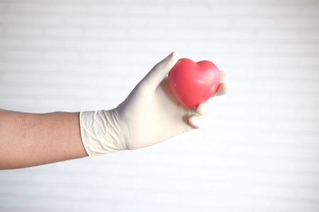 man hand in protective gloves holding red heart against white wall
