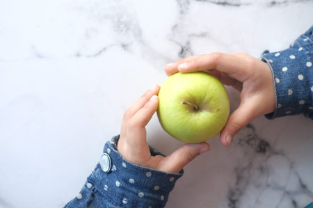 child girl hand holding green apple on tiles background