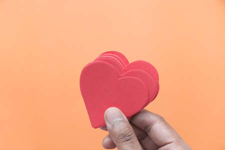 holding red heart on orange background top downの写真素材