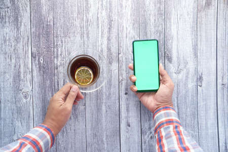 top view of young man hand using smart phone and drinking teaの写真素材