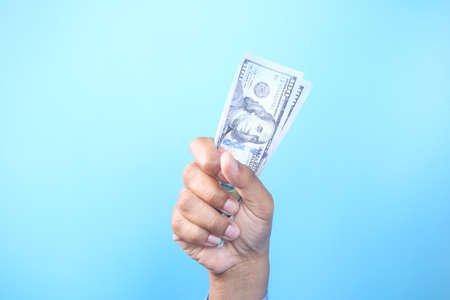holding 100 us dollar cash in hand against blue backgroundの写真素材