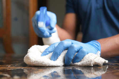 hand in blue rubber gloves holding spray bottle cleaning a table