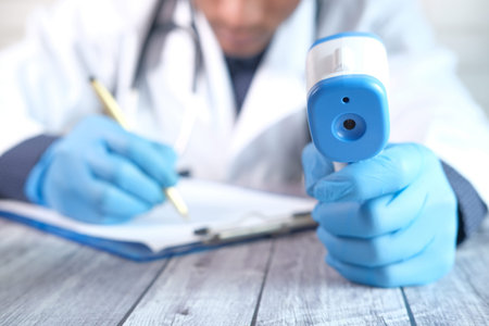 Hand holding infrared thermometer and writing on paper