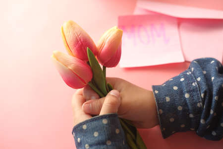 child hand holding tulip flower and mother day gift on tableの写真素材
