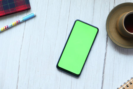 smart phone with empty screen, tea, notepad on wooden table