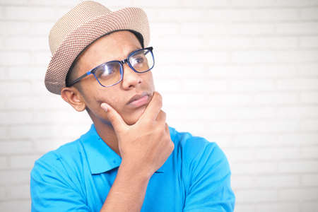 thoughtful young man with hat and eyeglass looking awayの写真素材