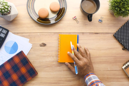 top view of man hand writing on notepad on office desk