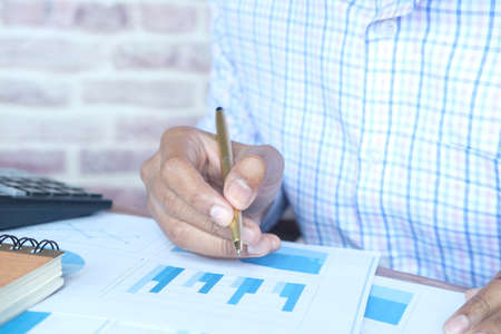 man hand with pen analyzing bar chart on paperの写真素材