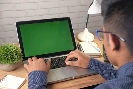 rear view of young man using laptop with blank screen on office desk.の写真素材