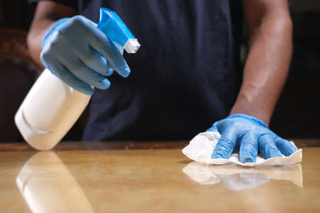 hand in blue rubber gloves holding spray bottle cleaning tableの写真素材