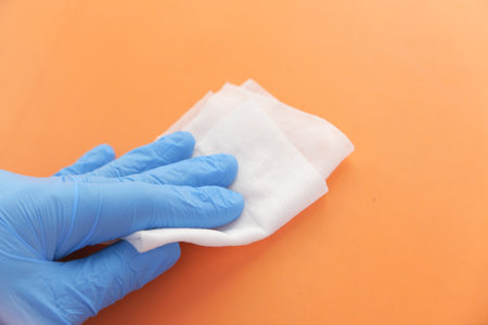 hand in blue rubber gloves cleaning table with clothの写真素材
