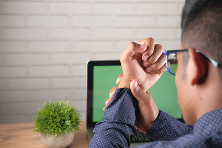Young man in suffering wrist pain working on laptop