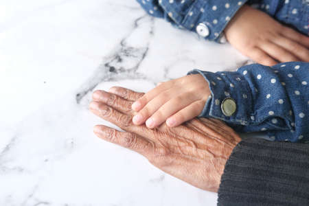 detail shot of child girl holding hand of a senior women on tableの写真素材