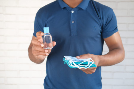 man hand holding surgical face mask and sanitizer gel