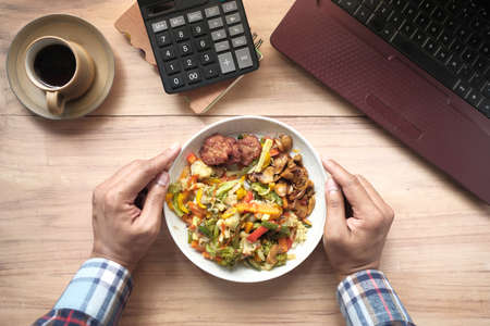 young man eating fresh salad while working on laptopの写真素材