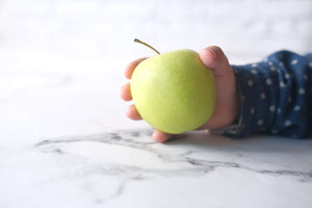 child hand holding green apple on white backgroundの写真素材