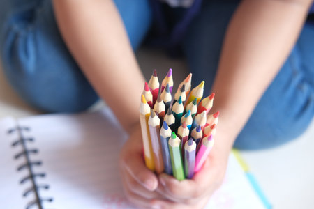 Close up of a child hand holding many colorful pencilsの写真素材