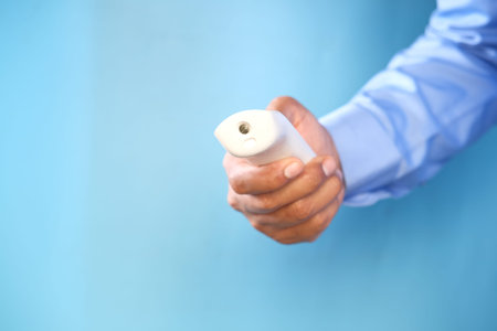 holding infrared thermometer to measuring temperature against blue background