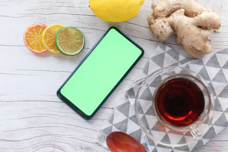 Top view of ginger tea and smart phone with green screen on wooden background.の写真素材