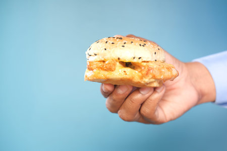 hand holding beef burger against blue backgroundの写真素材