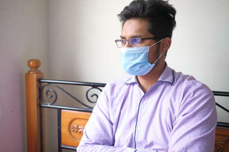 thoughtful young man with protective face mask sitting on bed looking awayの写真素材
