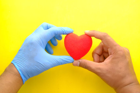 man hand in protective gloves holding red heart on yellow