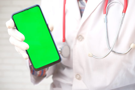 doctors hand in protective gloves holding smart phone with green screen