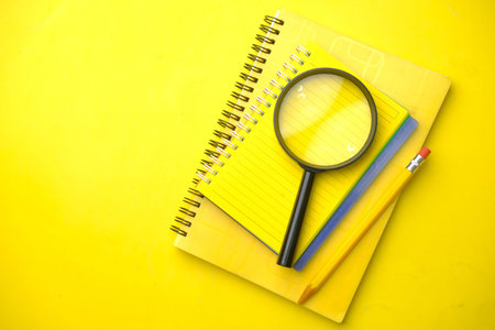 open book and magnifying glass on yellow background