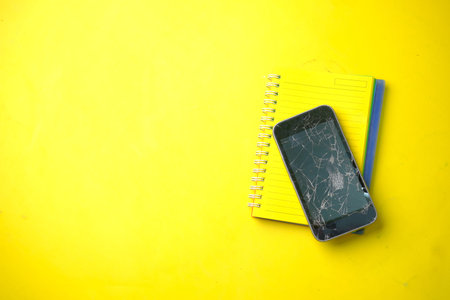 Top view of broken smart phone on yellow background