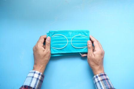 man hand holding surgical face mask on blue background ,の写真素材
