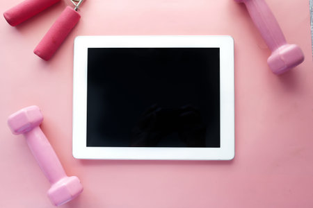 digital tablet with sports equipment on pink background