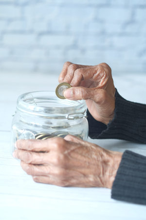 side view of senior women hand saving coins in a jar