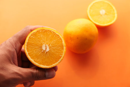 man hand holding slice of orange fruit i against blue background